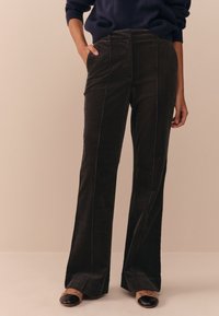 Pantaloni in velluto a coste scuro dal taglio dritto, con tasche frontali e cuciture verticali a contrasto. Indossati con ballerine nere.