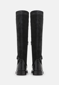 Bottes en suède noires jusqu'aux genoux avec des accents en cuir noir brillant, dotées d'une sangle avec une boucle de détail de chaque côté et d'une finition texturée.