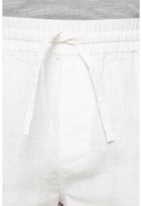 Shorts en lin blanc avec une taille à cordon, en tissu texturé et une poche avant. Tissu rayé gris visible au-dessus.