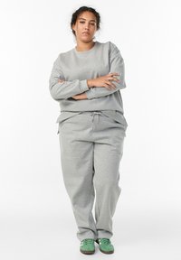 Light gray sweatshirt with ribbed cuffs and hem, paired with matching sweatpants featuring an elastic waistband and drawstring. Green sneakers.