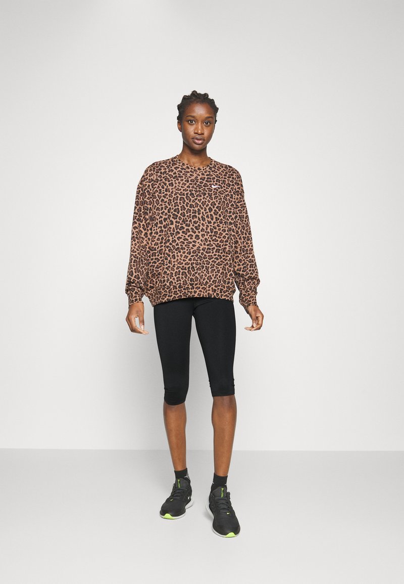 Felpa con stampa leopardata in marrone e nero, vestibilità rilassata con maniche lunghe, abbinata a pantaloni ciclisti neri e scarpe da ginnastica nere.