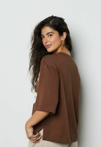 Tricou maro cu mânecă scurtă, croială lejeră, cu imprimeuri grafice colorate pe partea din față, gât rotund și deschideri laterale pentru confort.