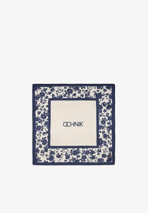 Kwadratowa biała apaszka z granatowym kwiatowym obramowaniem i granatowym ramieniem w środku, na którym widnieje nazwa marki w stylizowanych literach.