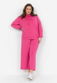 Felpa rosa con cappuccio e pantaloni larghi abbinati realizzati in un tessuto morbido, con una vestibilità comoda e dettagli coulisse sul cappuccio.