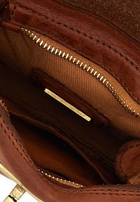 Interno di una borsa in pelle marrone con una tasca con cerniera e dettagli in metallo dorato, texture liscia e fodera in tessuto color cognac.