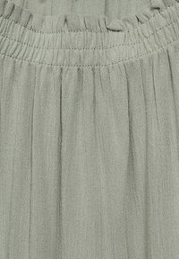 Lichtgrijze stof met een gestructureerde afwerking, voorzien van een geplooide en elastische tailleband, die zachte plooien door het materiaal creëert.