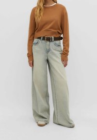 Suéter marrón de manga larga combinado con jeans ligeros de pierna ancha. Los detalles incluyen un cinturón marrón y calzado beige. Diseño sencillo, textura suave.
