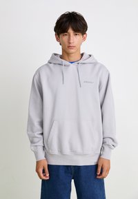 Hoodie gris clair en coton, doté d'une poche kangourou à l'avant et d'une capuche avec cordon de serrage. Le vêtement a une coupe décontractée et des poignets côtelés.