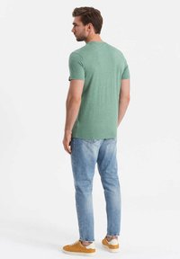 Camiseta verde de manga corta en una tela suave y texturizada, combinada con jeans azul claro y zapatillas amarillas. Presenta un cuello redondo clásico.