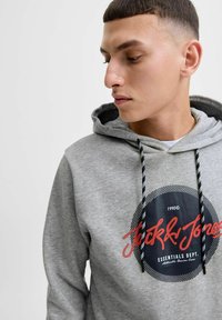 Gray hoodie with a round logo featuring "Jack & Jones" in red script. Textured fabric with contrasting black and white drawstrings.