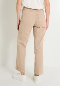 Pantalones beige de corte recto, con bolsillos traseros visibles, dobladillo vuelto y textura de tela. Combinados con zapatillas blancas.