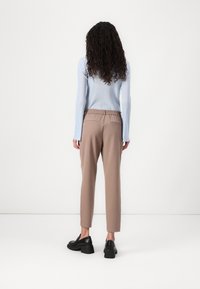 Un haut à manches longues côtelé bleu clair et un pantalon beige fuselé avec une taille élastique, des chaussures noires à enfiler, présentés de dos.