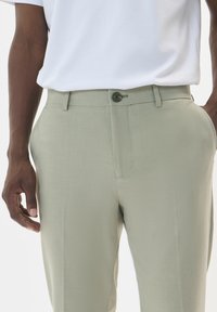 Light green trousers made of textured fabric, featuring a front button closure, belt loops, and side pockets. Paired with a white t-shirt.