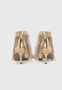 Gold high-heeled shoes with fringe detailing at the back. Made of shiny metallic material, featuring a sleek stiletto heel and an ankle strap.
