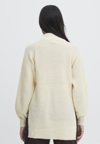 Cremefarvet striktrøje med en afslappet pasform, der har lange ærmer og en ribbet struktur. Bagsiden har et subtilt høj-lav kantdesign.