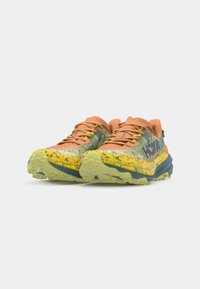 Zapatillas deportivas en naranja, amarillo y verde azulado, con una parte superior texturizada, una entresuela estampada y una suela exterior rugosa en verde. Presenta un logotipo destacado.