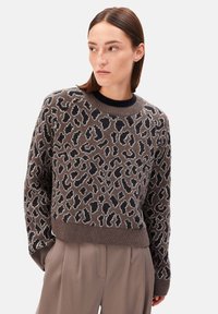 Brauner Strickpullover mit Leopardenmuster in Schwarz und Beige. Hat einen Rundhalsausschnitt sowie gerippte Bündchen und Saum. Glatte Textur, Pulli-Stil.