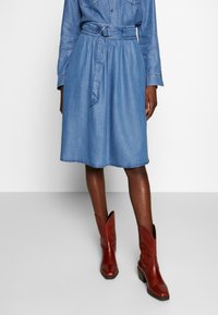 Jeansklänning med insvängd midja, featuring ett bälte med en rund spänne, knälång, i ljusblått, kombinerad med röda ankelstövlar.