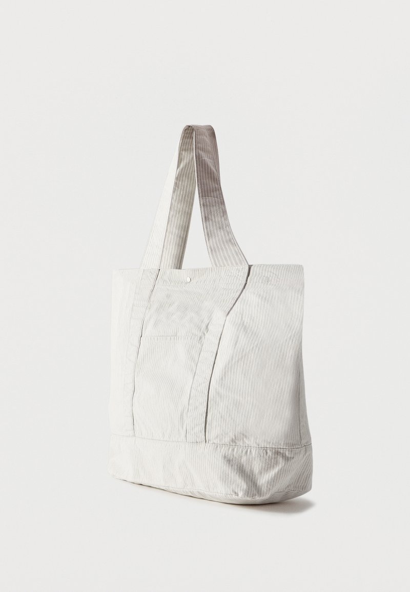 Off-white, grote stoffen draagtas met dubbele handgrepen en subtiele verticale strepen, rechtopstaand op een effen witte achtergrond.