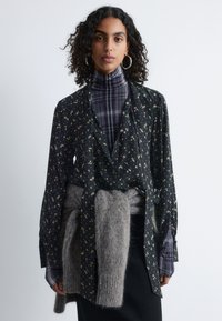 Floral black blouse with long sleeves, featuring a tie at the waist. Worn over a purple plaid turtleneck, paired with a gray wool sweater.