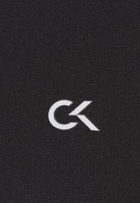 Tissu noir à texture côtelée arborant un logo Calvin Klein blanc bien visible. Le design est simple et minimaliste.