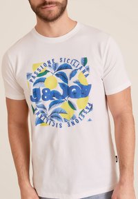 Witte katoenen t-shirt met een blauwe grafische print van citroenen, groene bladeren en de tekst "J&JOY PASSIONE SICILIANA" in het blauw.