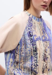 Κοντομάνικο τοπ με μοτίβο σε μωβ και μπεζ αποχρώσεις, με στρογγυλή λαιμόκοψη και αντίθετα μανίκια από κρεμ ύφασμα που μοιάζει με μετάξι.