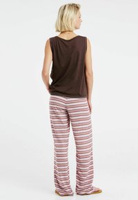 Top sin mangas marrón con escote redondeado, combinado con pantalones de pierna ancha de rayas rojas y blancas, con un sutil diseño de zigzag.