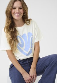 T-shirt crème avec un grand motif "love" en bleu, à manches courtes, coupe décontractée, associé à un pantalon texturé bleu marine.
