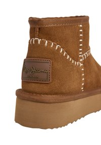 Brūni zamšādi potīšu zābaki ar baltu aizšuvumu, biezu zoli un "Pepe Jeans London" ādas etiķeti uz aizmugurējā papēža.