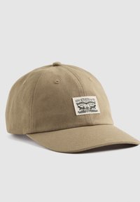 Cappellino da baseball color khaki in cotone, con un patch cucito con grafiche e testo sul davanti, visiera curva e cinturino posteriore regolabile.