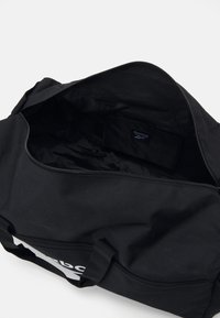 Geantă de voiaj neagră cu exterior dintr-un material textil neted, cu închidere cu fermoar și un interior încăpător dotat cu o etichetă. Mânere scurte din țesătură pentru o transportare ușoară.