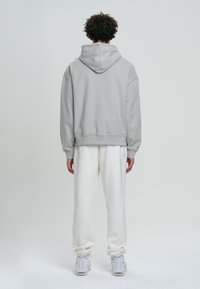 Felpa grigia chiara con cappuccio, dal taglio rilassato, con polsini e orlo a coste. Abbinata a pantaloni della tuta color crema e sneakers bianche.