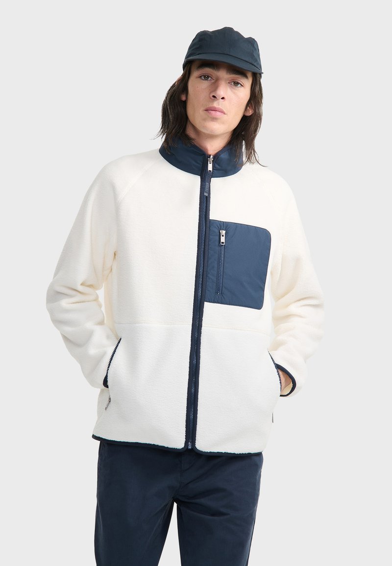 Fleecejacke in Creme mit marineblauen Akzenten. Verfügt über einen hohen Kragen, Reißverschlusstaschen und eine kontrastierende Brusttasche. Weicher Stoff und lockere Passform.