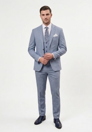 Hombre con traje de tres piezas azul claro, camisa blanca, corbata estampada y zapatos de vestir negros, de pie frente a un fondo blanco liso.