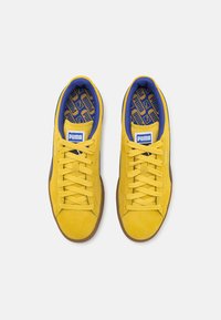 Gule semskede sneakers med blå kant, gummisål og flade snørebånd. Bemærkelsesværdig mønstret indersål har geometriske designs.