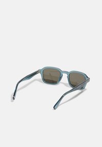 Tyrkise sunglasses med firkantede rammer, mørkebrune linser og slanke armer med metalliske detaljer. Glatt tekstur, lett design.