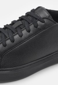 Baskets en cuir noir avec une finition texturée, bout rond, lacets plats noirs et semelle en caoutchouc. Présentent des détails de couture contrastants.