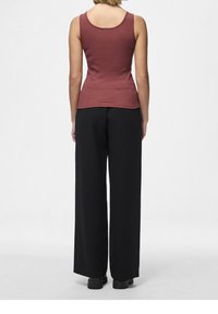 Top in tinta bordeaux a coste con scollatura sul retro, abbinato a pantaloni neri a gamba larga e scarpe nere, mostrato da dietro.