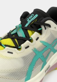 Asics FujiSpeed 4 futócipő fehér, fekete és élénk türkiz színben. Jellemzői a texturált hálós felsőrész, élénk sárga kiegészítők és mintás fűzők.