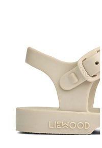 Vaaleabeige kumi sandaali, jossa on kuvioitu pohja, säädettävä solkisäädin ja kohokuvioitu brändilogolla "LIEWOOD" jalan alla.
