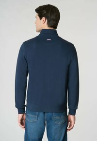 Felpa a collo alto di colore navy realizzata in tessuto morbido, presenta polsini e orlo a costine, con un piccolo logo del brand sul collo.