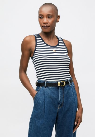 Stripet tank topp i marineblått og hvitt med rund hals, kombinert med høyt liv denim-bukser og et svart belte med gullspenne.
