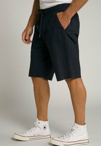 Marineblaue Shorts mit einem Kordelzugbund, seitlichen Taschen und einer lässigen Passform, kombiniert mit weißen High-Top-Sneakern.