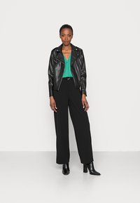 Jaqueta de motoqueiro de couro preta sobre uma blusa verde com decote em V, combinada com calças largas pretas e botas ankle texturizadas pretas.