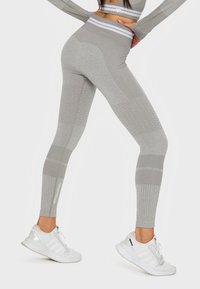 Hochtaillierte graue Leggings mit texturierten Mustern und gerippten Details; beinhaltet einen weißen Logo-Akzent und passt zu weißen Sportschuhen.