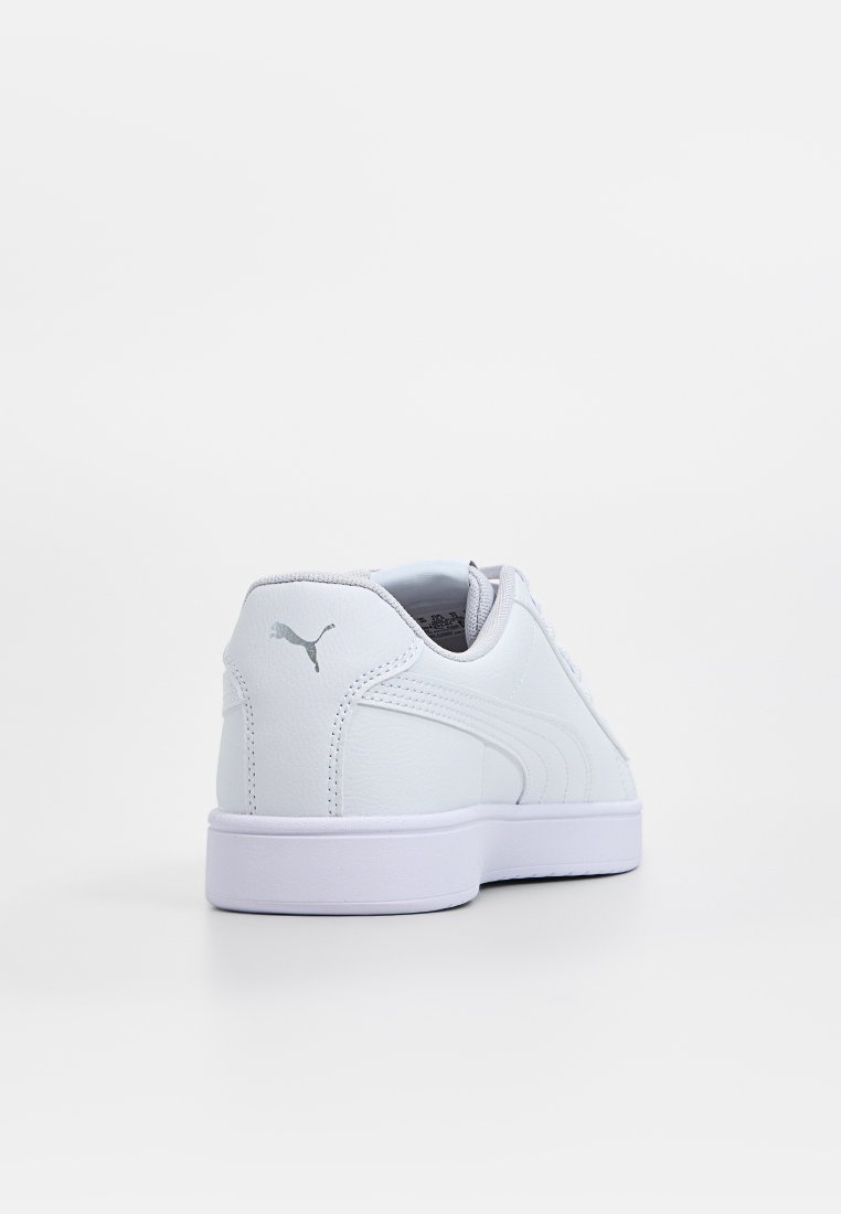 Zapatilla sintética blanca con un acabado suave, forma redondeada, diseño de caña baja y un acento de logo gris en el talón. Suela de goma plana.