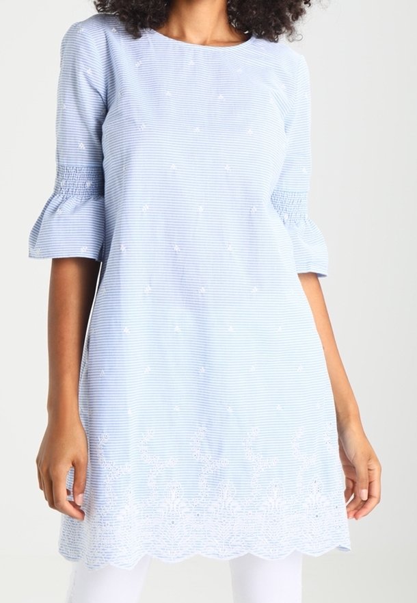 Tunique rayée bleu clair avec manches bouffantes, ornée de broderies florales et d'un détail d'ourlet festonné. Fabriquée en tissu respirant.