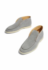 Zapatos slip-on de ante gris con una textura suave, puntera redondeada y costuras mínimas. Suela de color crema con un ligero arco para mayor comodidad.