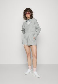 Sweatshirt cinzento curto com um logo, combinado com uma mini saia de cordão a condizer. Usado com ténis brancos e meias rosas, acessorizado com óculos de sol cor-de-rosa.